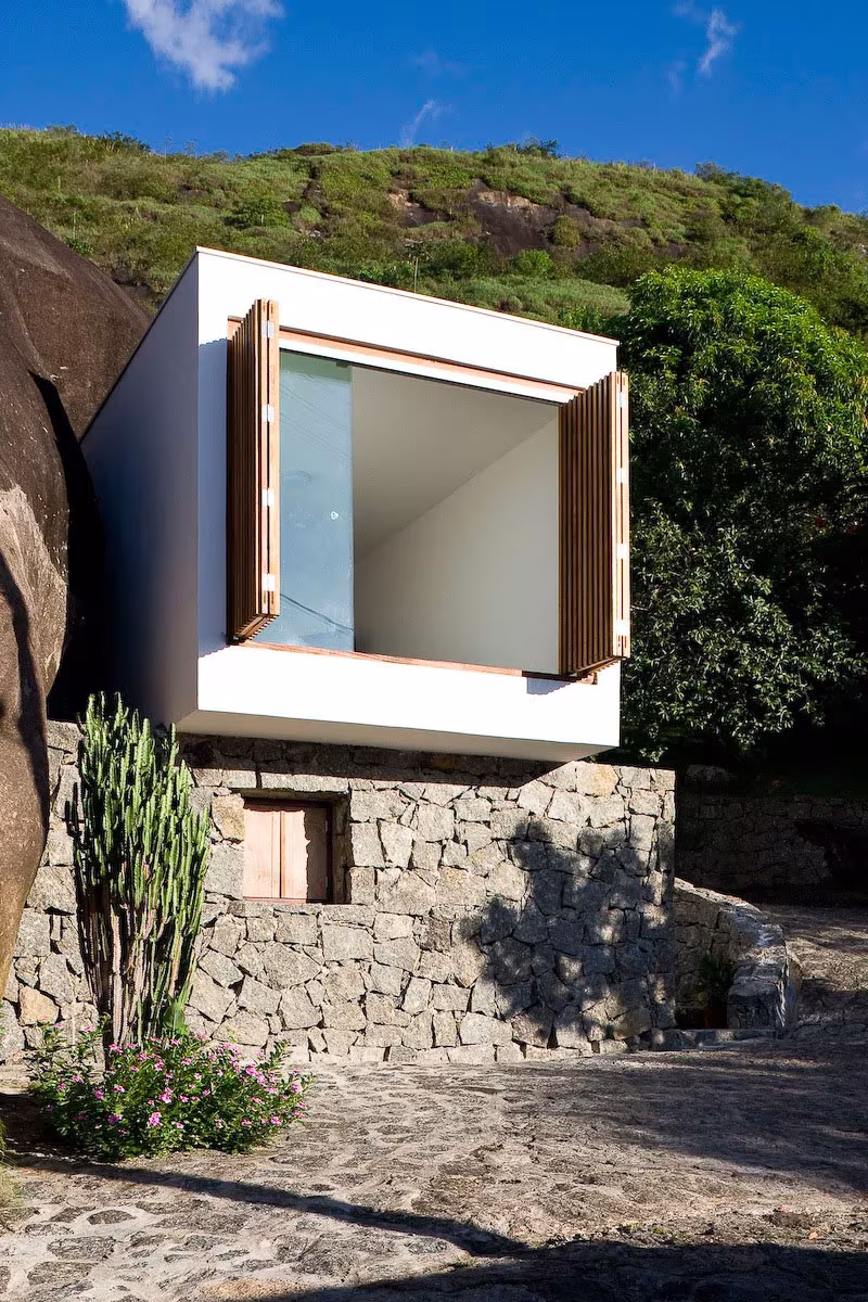 Box House con las contraventanas de madera de la caja abiertas, sobre muros de piedra y entre vegetación