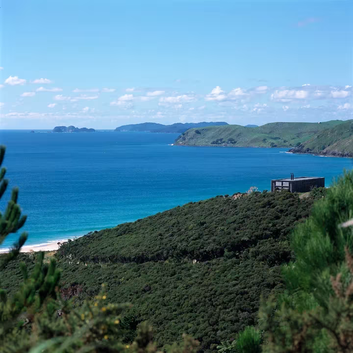 Vista de la costa de Coromandel desde la colina, con bahía azul, playa e islas, y la cabaña entre arbustos