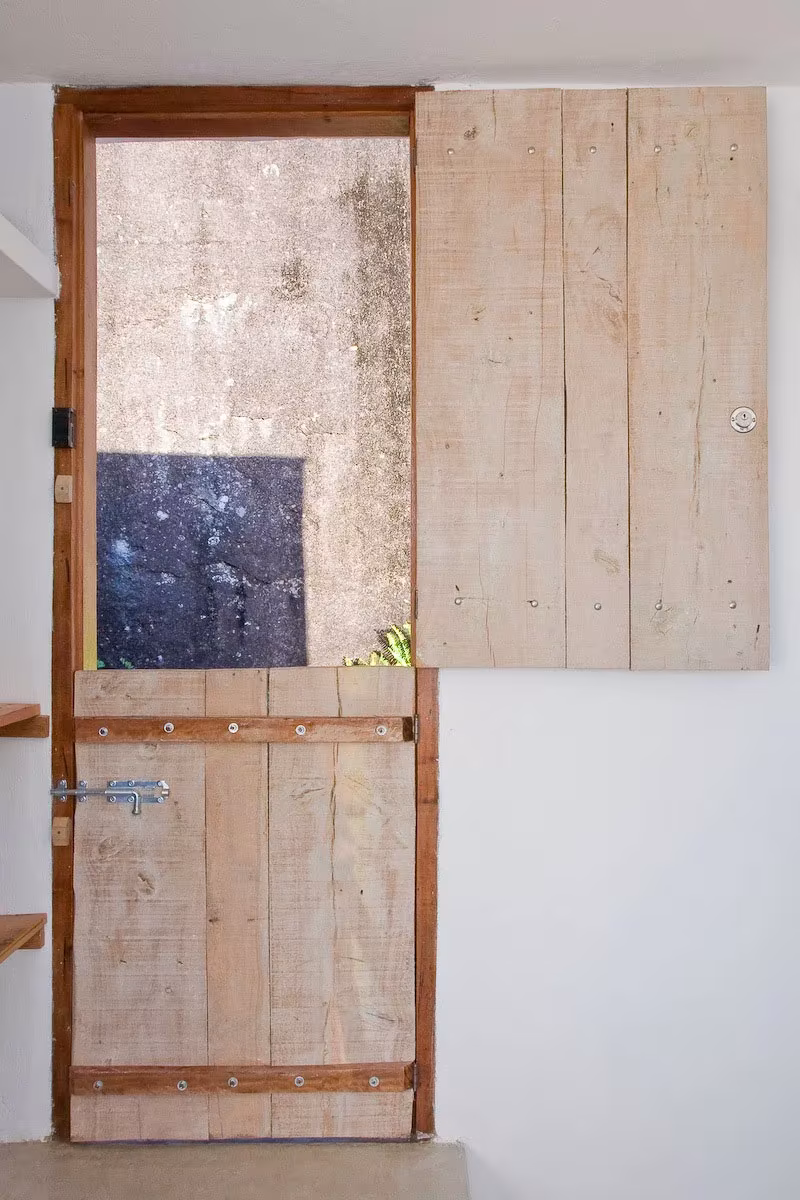Puerta de tablas de madera recuperada con ventanuco, en una pared blanca de la Box House