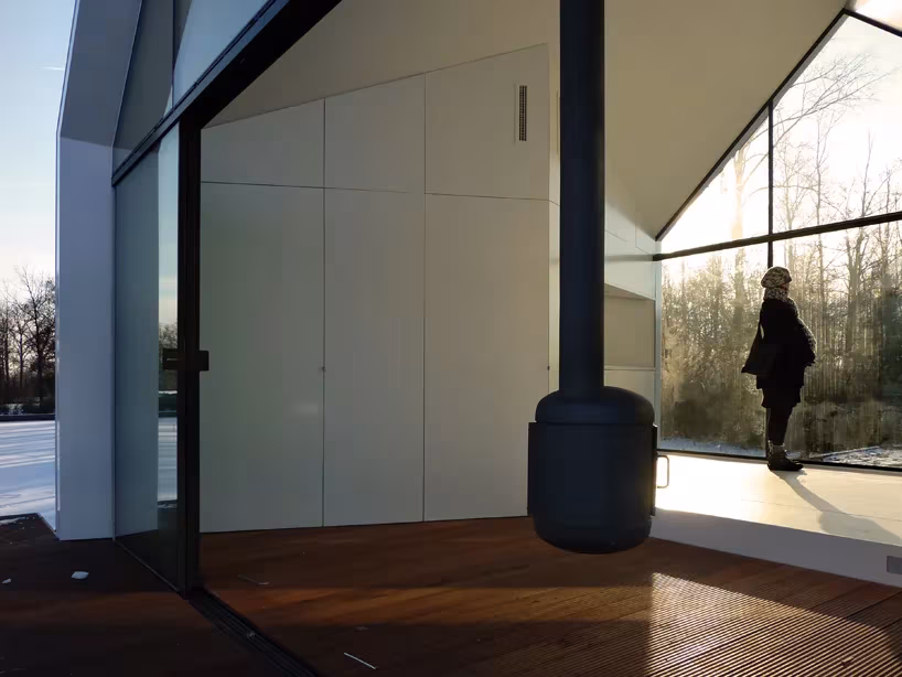 Casita de fin de semana de 2by4 architects en Loosdrecht: estufa central y ventanal con una persona mirando el lago
