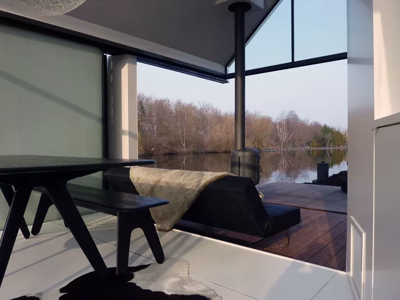 Mesa negra y sofá junto al ventanal de esquina que se abre al lago Loosdrecht en la casita de 2by4