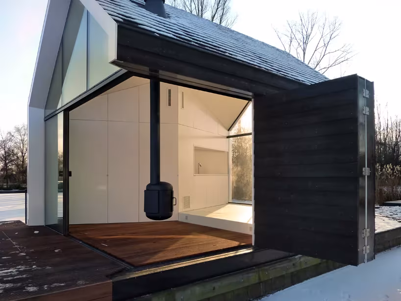 Esquina de la casita de Loosdrecht abierta a la terraza de madera, con estufa negra suspendida en el interior