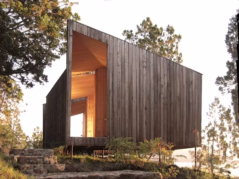 Volumen inclinado de tablas de madera oscura con abertura luminosa en la sauna de Panorama Arquitectos