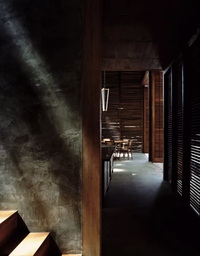 Casa Palmyra de Studio Mumbai: pasillo en penumbra con luz rasante sobre un muro de estuco y celosías de madera