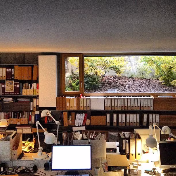 Estudio de ÁBATON con mesas de trabajo, flexos, estanterías con archivadores y ventana corrida al jardín