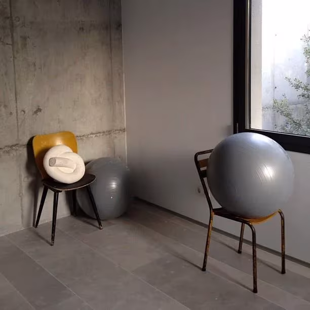 Dos sillas vintage con pelotas de pilates grises junto a una ventana en un espacio de hormigón visto