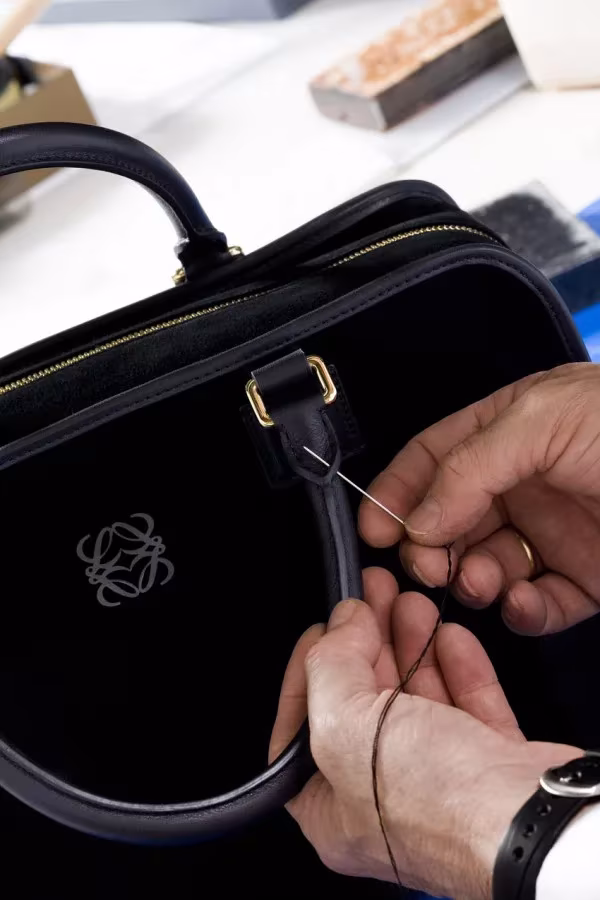 Manos de un artesano cosiendo el asa de un bolso Amazona negro en los talleres de Loewe