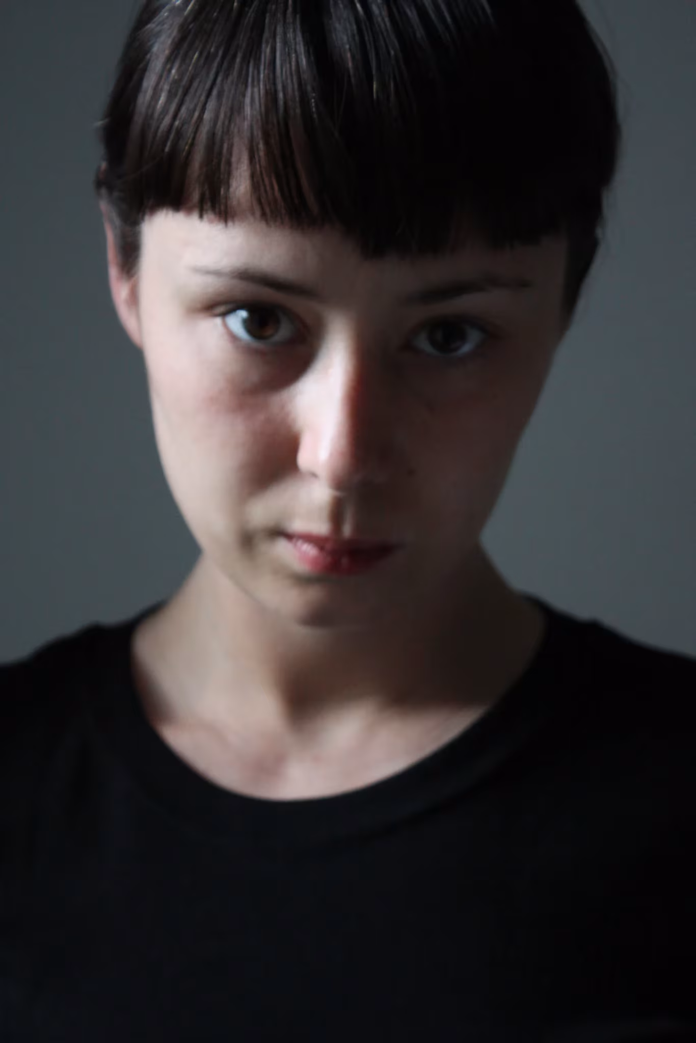 Retrato de la diseñadora Tachy Mora, mujer joven de flequillo con camiseta negra sobre fondo gris