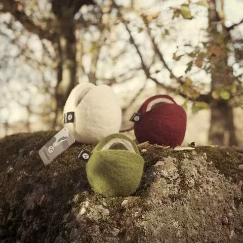 Cestos de fieltro en blanco, granate y verde sobre una roca con musgo en un bosque soleado