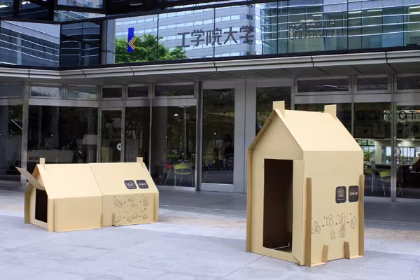 Refugios de cartón de Atelier OPA montados frente a la entrada acristalada de una universidad en Japón