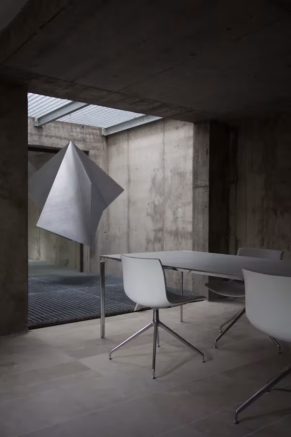 Sala de reuniones de hormigón visto en la oficina de ÁBATON, con mesa blanca y lámpara de papel facetada