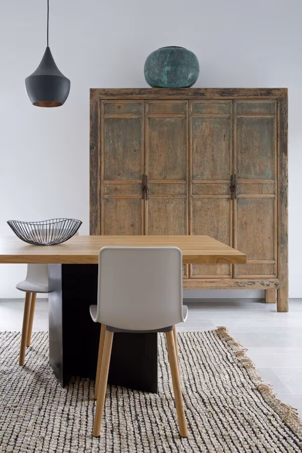 Rincón de comedor de la oficina de ÁBATON con armario antiguo de madera, mesa de roble y alfombra de yute