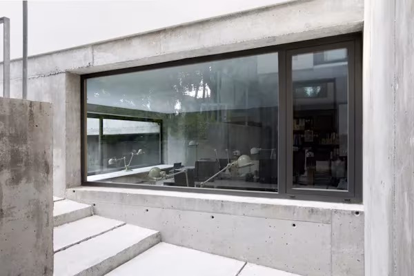 Fachada de hormigón visto de la oficina de ÁBATON con ventana alargada de carpintería negra y escalones