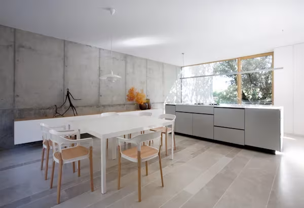 Cocina comedor de la oficina de ÁBATON con muros de hormigón, isla gris y mesa blanca con sillas de madera