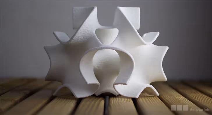 Figura de azúcar impresa en 3D con puntas y arcos simétricos, sobre tarima de madera