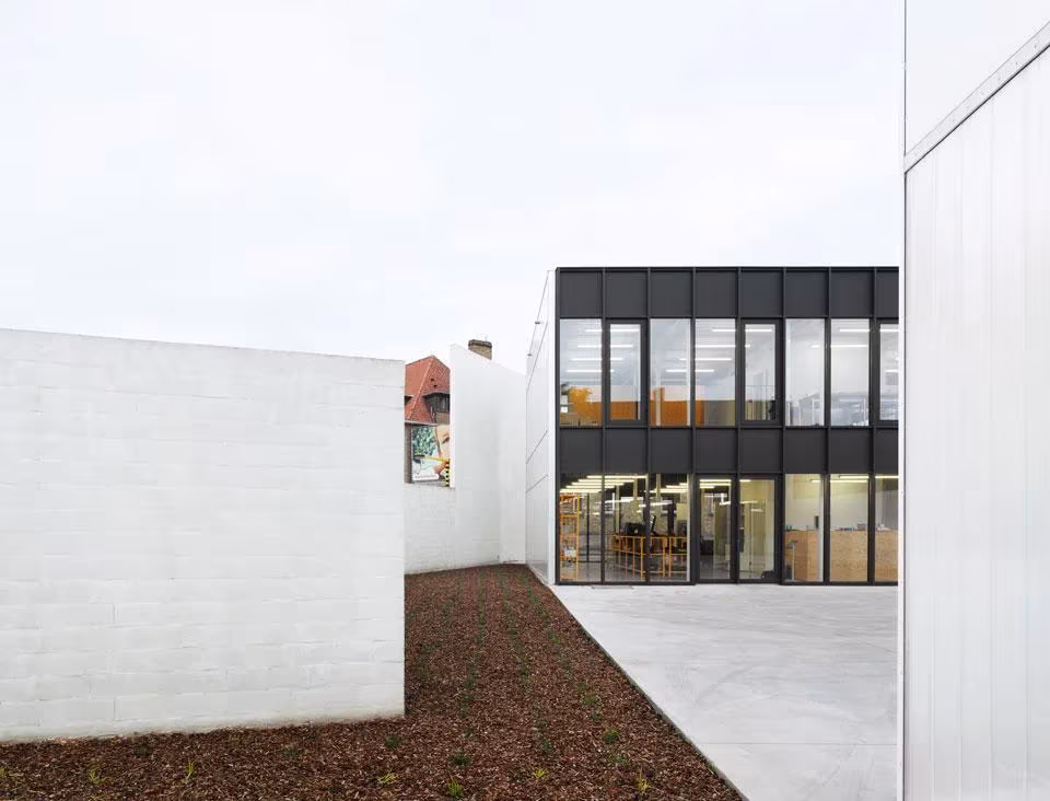 Patio entre muros blancos frente a un edificio acristalado de la oficina de Tielt