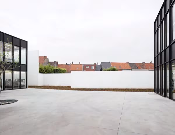Amplio patio de hormigón cerrado por muros blancos entre los dos edificios de la oficina en Tielt