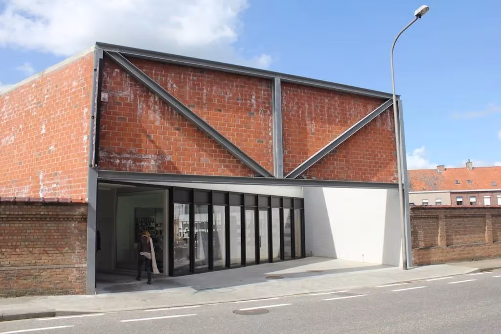 Fachada de ladrillo con cruces de acero y planta baja acristalada de la oficina en Tielt