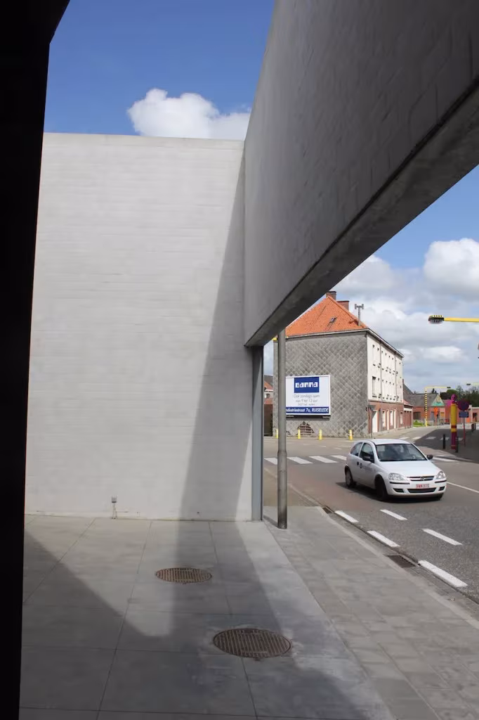 Muro blanco de la oficina en Tielt que enmarca la calle, con un coche pasando y cielo azul