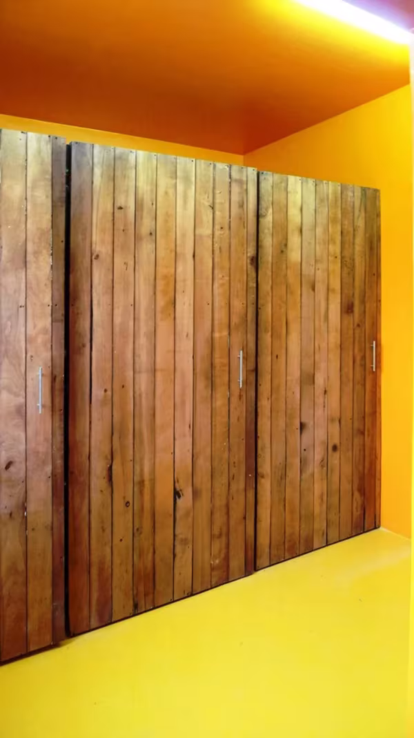 Puerta de tablones de madera envejecida en un pasillo pintado de amarillo intenso en el Hostal Caracol
