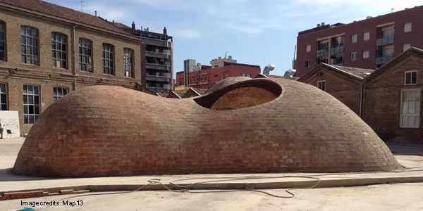 Cúpula de ladrillo de Bricktopia con un óculo superior, entre edificios de ladrillo en Barcelona