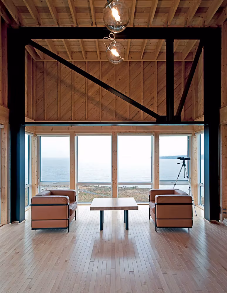 Salón de la casa en el acantilado con techo de madera, estructura de acero negra y ventanal al mar