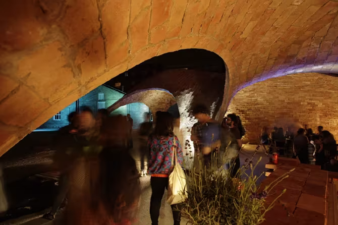 Personas en movimiento bajo la bóveda iluminada del pabellón Bricktopia durante un evento nocturno