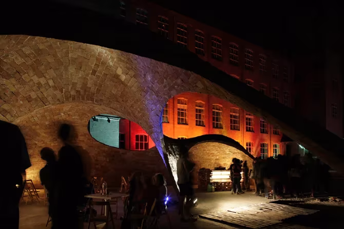 Bóvedas de ladrillo de Bricktopia iluminadas en rojo y naranja de noche, con siluetas de visitantes