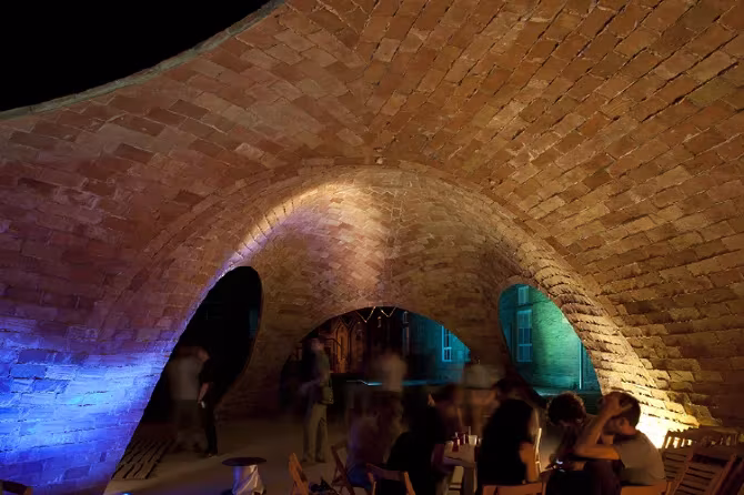 Arcos de ladrillo de Bricktopia bañados de luz azul y ámbar sobre un grupo reunido de noche