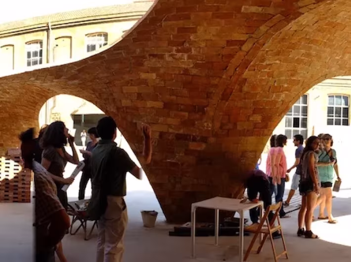 Visitantes bajo los arcos de ladrillo del pabellón Bricktopia en una jornada a pleno sol