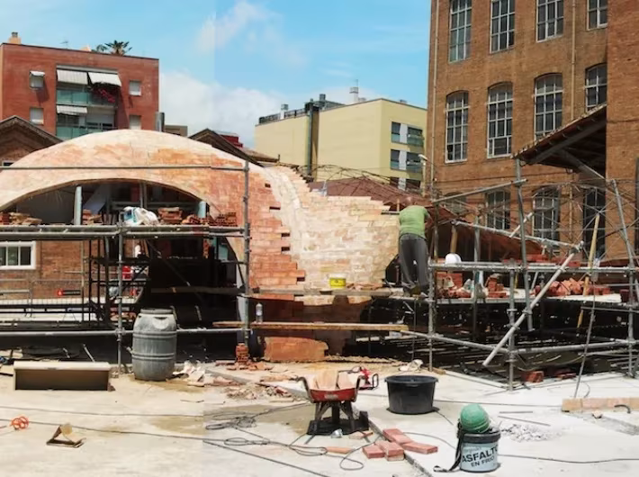 Bóveda de ladrillo de Bricktopia en obra, rodeada de andamios, carretillas y cubos