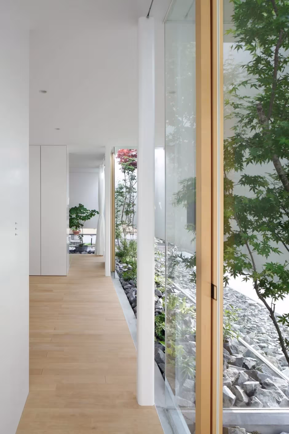 Corredor blanco de la Green Edge House con puerta corredera de vidrio abierta al jardín de piedras