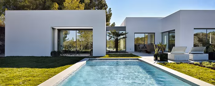 Villa blanca de ÁBATON en Las Colinas con piscina alargada, césped y ventanales al jardín