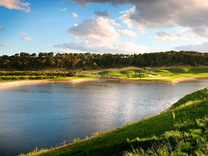Lago del campo de golf de Las Colinas rodeado de césped y vegetación bajo un cielo azul