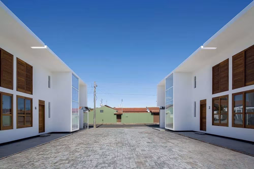 Patio colectivo adoquinado entre los dos bloques blancos con contraventanas de madera de las Casas AV