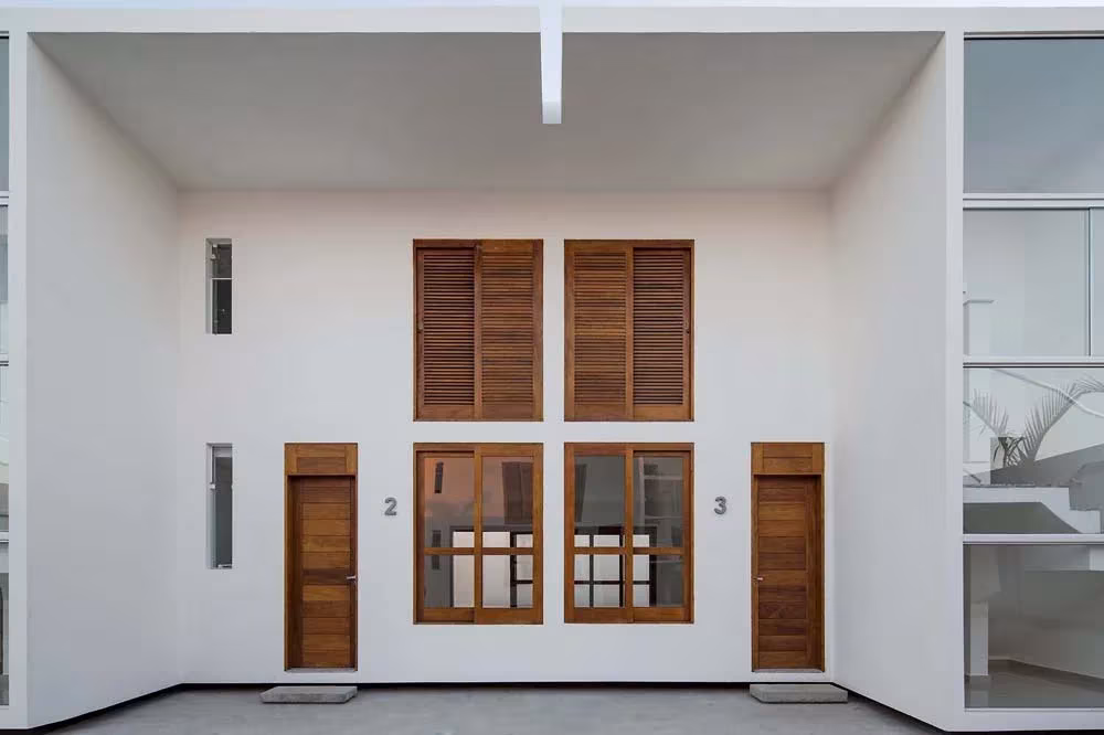 Fachada blanca de dos viviendas de las Casas AV con puertas y contraventanas de madera
