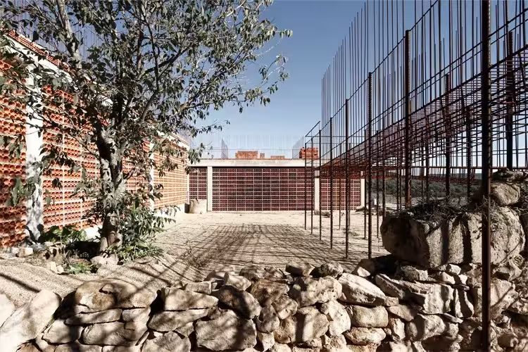 Patio del dolmen de Seró de Toni Gironés con muro de piedra seca, árbol y estructura de varillas de acero