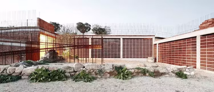 Edificio bajo de celosía cerámica y piedras en el jardín del Espacio Transmisor del dolmen de Seró