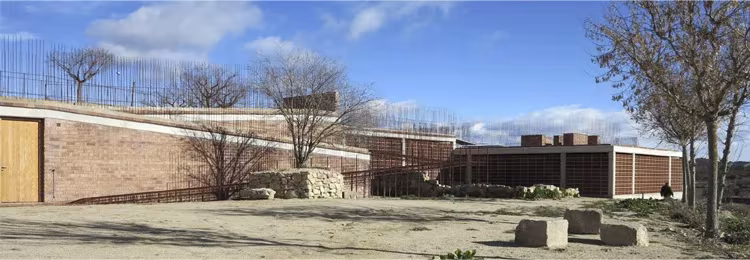 Vista panorámica del edificio de ladrillo del dolmen de Seró integrado en el terreno, con árboles sin hojas