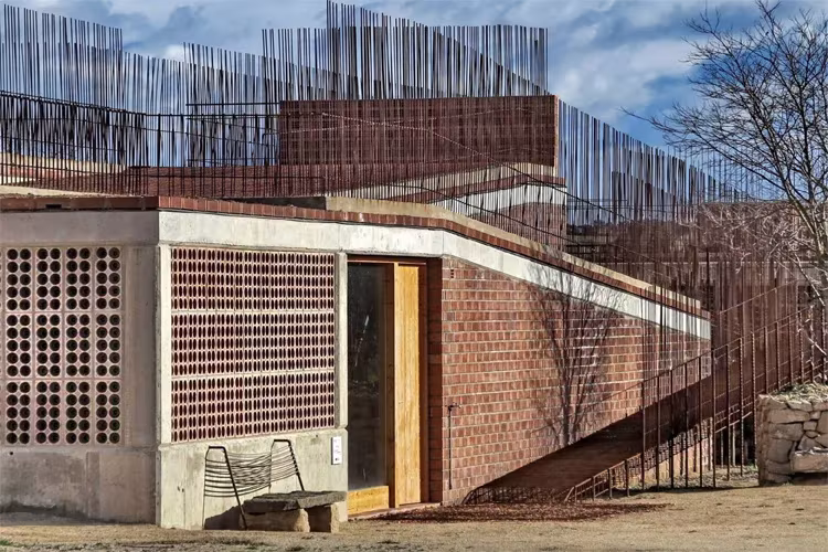 Esquina de hormigón y celosía cerámica del edificio de Seró, con banco y rampa de varillas de acero