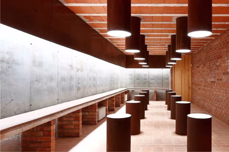 Sala con muro de hormigón, banco corrido de ladrillo y taburetes cilíndricos de acero corten en Seró