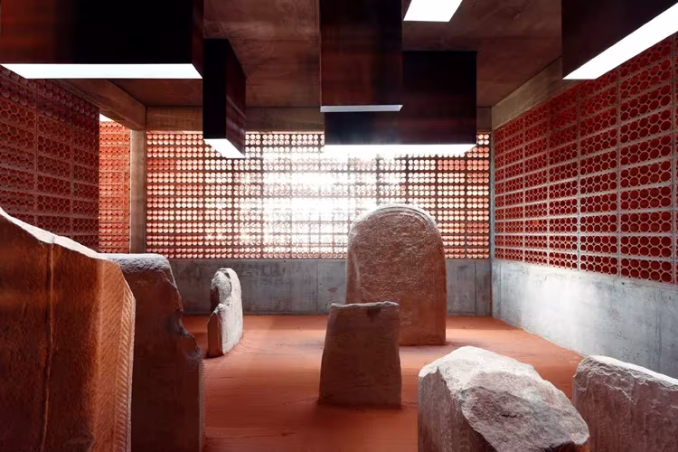 Sala del túmulo de Seró con piedras del dolmen sobre suelo rojo, entre celosías y luz cenital