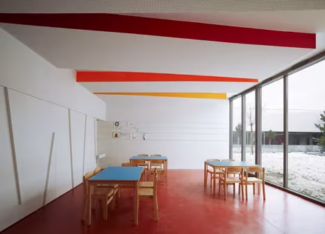Sala luminosa de las Escuelas Josephine Baker con mesas azules, sillas de madera y fachada acristalada
