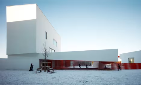 Patio nevado de las Escuelas Josephine Baker con volúmenes blancos voladizos y niños jugando
