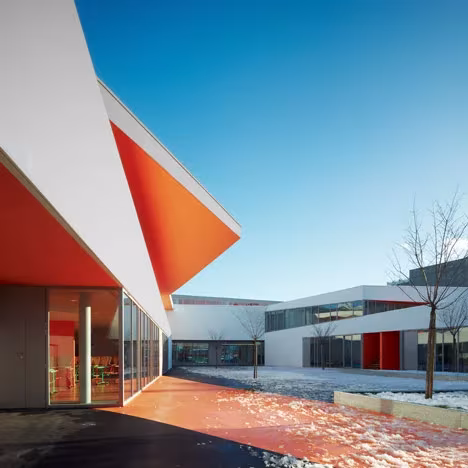 Esquina de las Escuelas Josephine Baker con voladizo naranja en punta y patio con restos de nieve