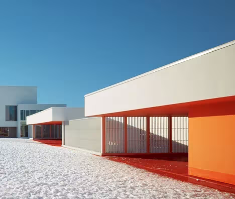Porche naranja bajo un volumen blanco de las Escuelas Josephine Baker frente a un patio nevado