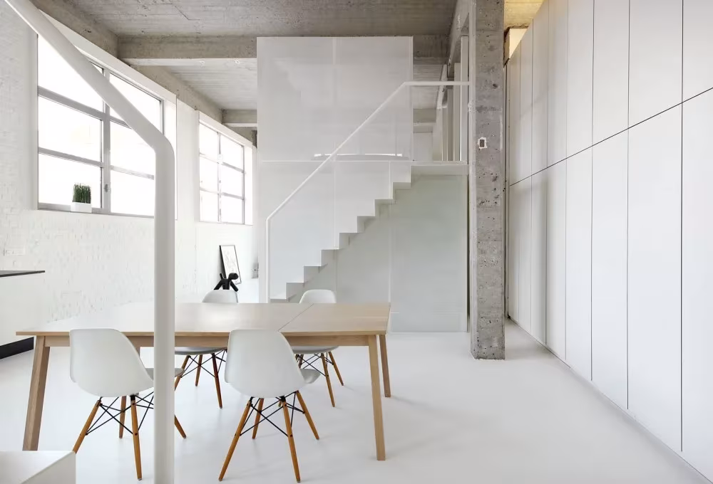 Comedor del Loft For con sillas blancas, escalera ligera y pilar de hormigón visto