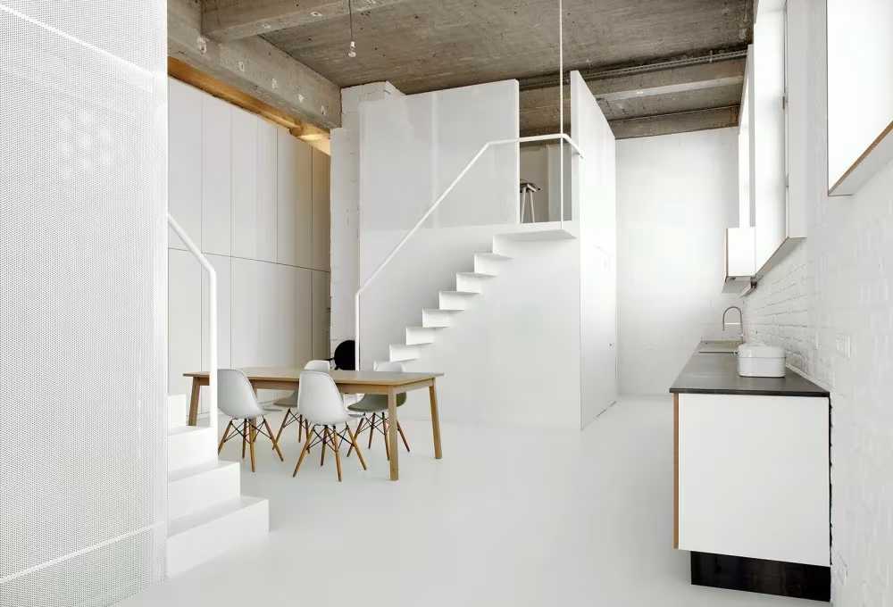 Interior blanco del Loft For con escalera hacia el volumen superior, mesa de comedor y cocina
