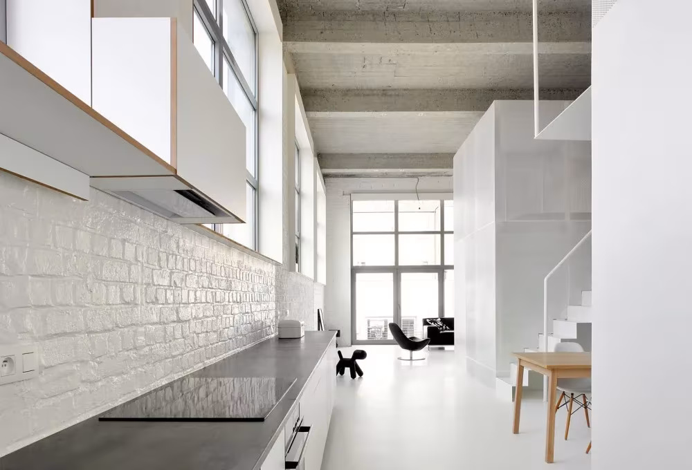 Cocina del Loft For con pared de ladrillo pintado de blanco y encimera negra, hacia los ventanales