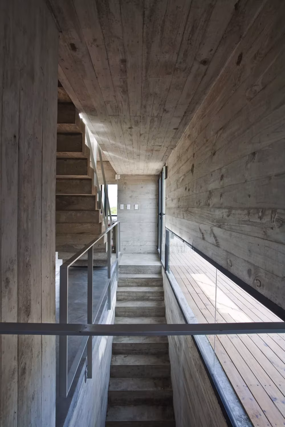 Escalera estrecha entre muros de hormigón encofrado con tablas en la Casa en la Playa de BAK Arquitectos